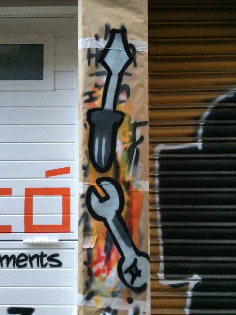 graffiti decorativo de herramientas pintado a mano en columna de fachada de lampistería en Barcelona