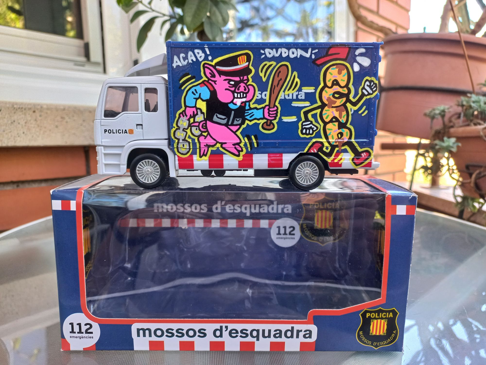 Miniatura de furgoneta de los Mossos d'Esquadra personalizada con graffiti, presentada en su caja original como pieza de colección de stuffcustoms.